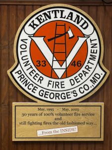 A wooden plaque for Kentland Volunteer Fire Department, Prince George’s Co., MD, features a large "V" with a ladder and axe. Below, a sign reads: “May, 1995 — May, 2025, 30 years of 100% volunteer fire service… From the INSIDE!”.