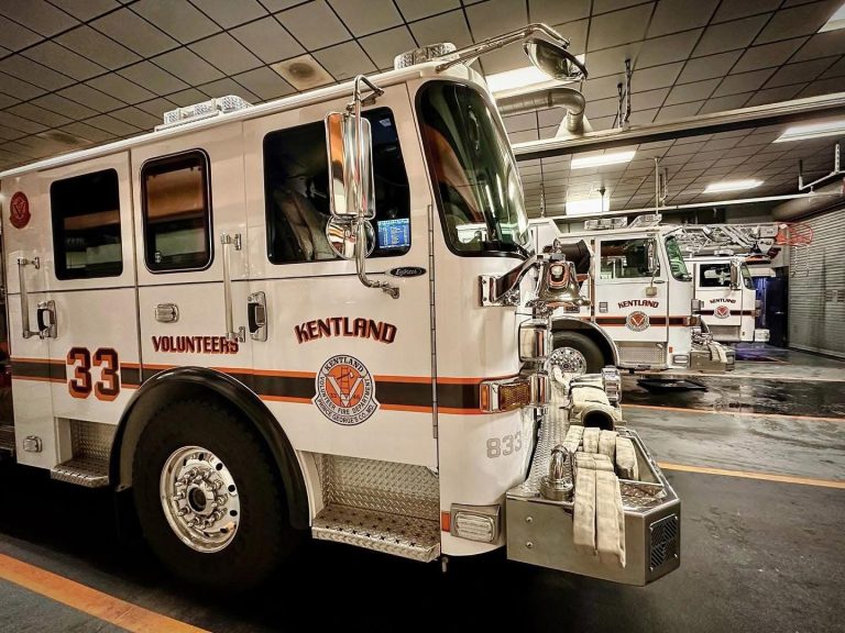 A row of white Kentland Volunteer fire trucks, labeled with the number 33, parked inside a fire station garage under bright ceiling lights.